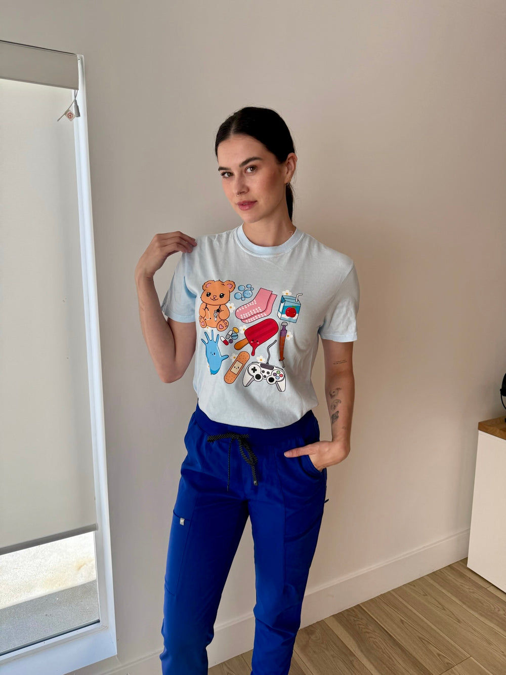 Scrubhacks wearing the light blue Ladyspinedoc x Scrubhacks Pediatric Nurse Collage Tee Shirt 
