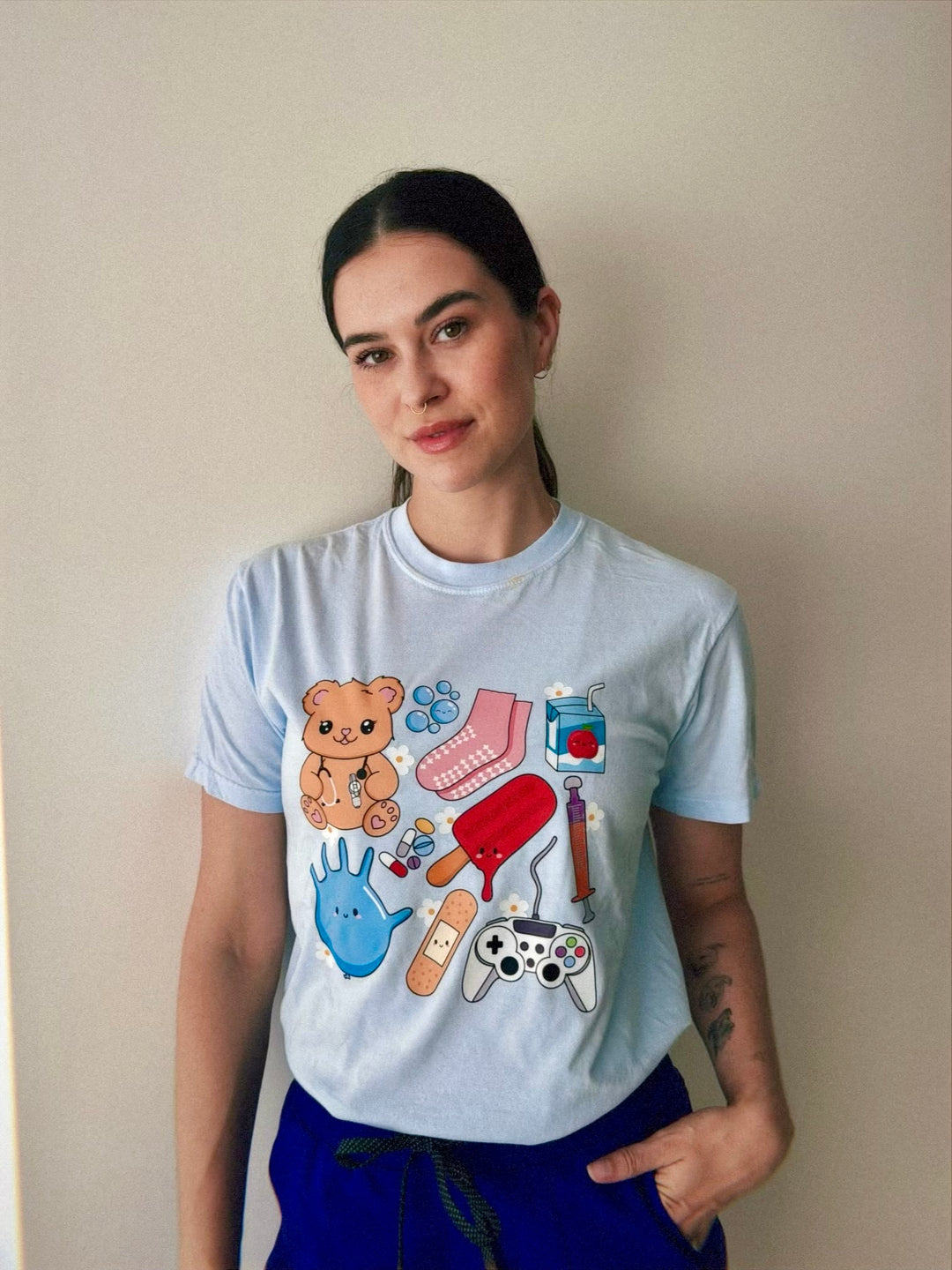 Close up of Scrubhacks wearing the light blue Ladyspinedoc x Scrubhacks Pediatric Nurse Collage Tee Shirt 