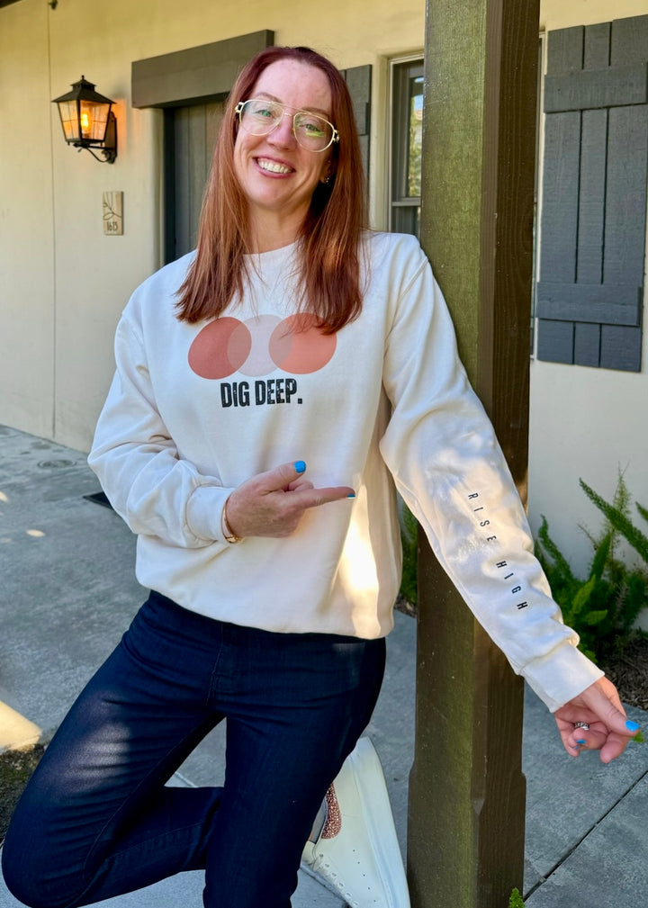 Ladyspinedoc wearing a cream sweatshirt with Dig Deep graphic design and Rise Up sleeve text, standing outdoors.
