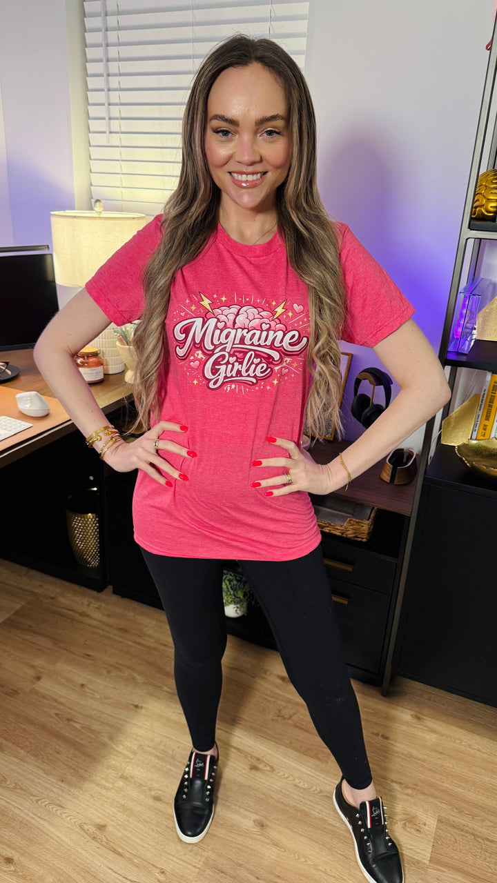 Dr. Jessica Lowe wearing a pink t-shirt with Migrain Girlie text, standing in an indoor setting.
