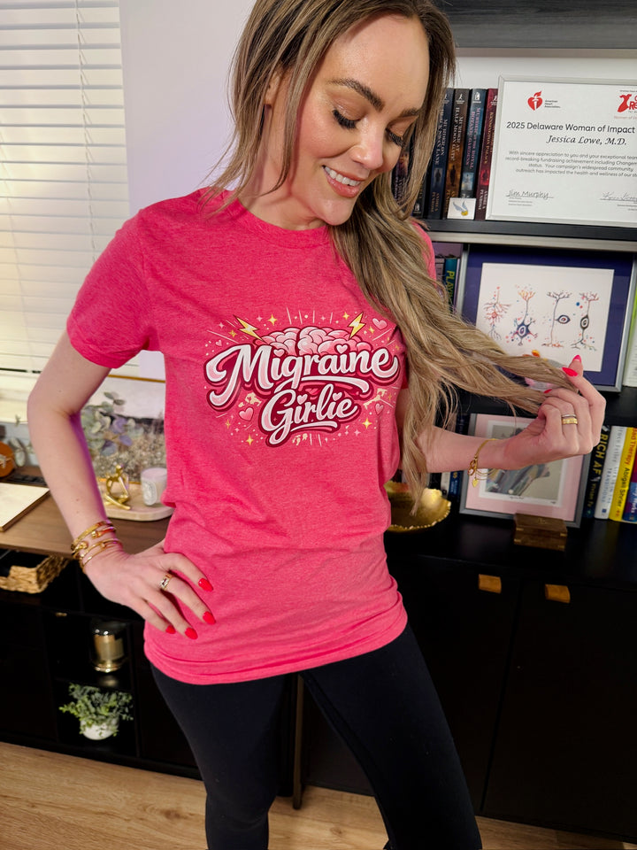 Dr. Brain Barbie wearing a pink 'Migraine Girlie' t-shirt in an office setting.