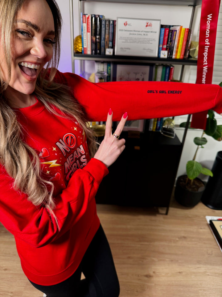 Dr. Brain Barbie wearing a red No Mean Girls sweatshirt in front of a bookcase and showing off the Girl's Girl Energy sleeve art