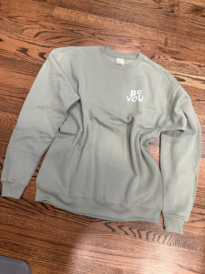 Sage green Be You sweatshirt with text on a wooden floor