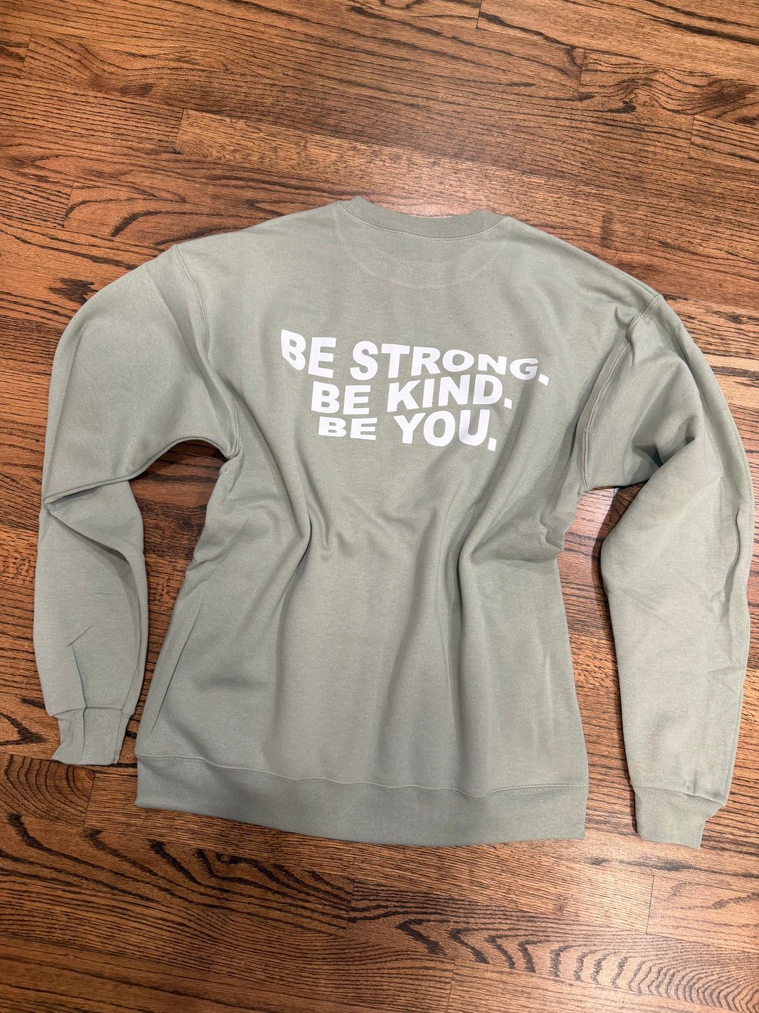 Sage green Be You sweatshirt with motivational text on a wooden surface