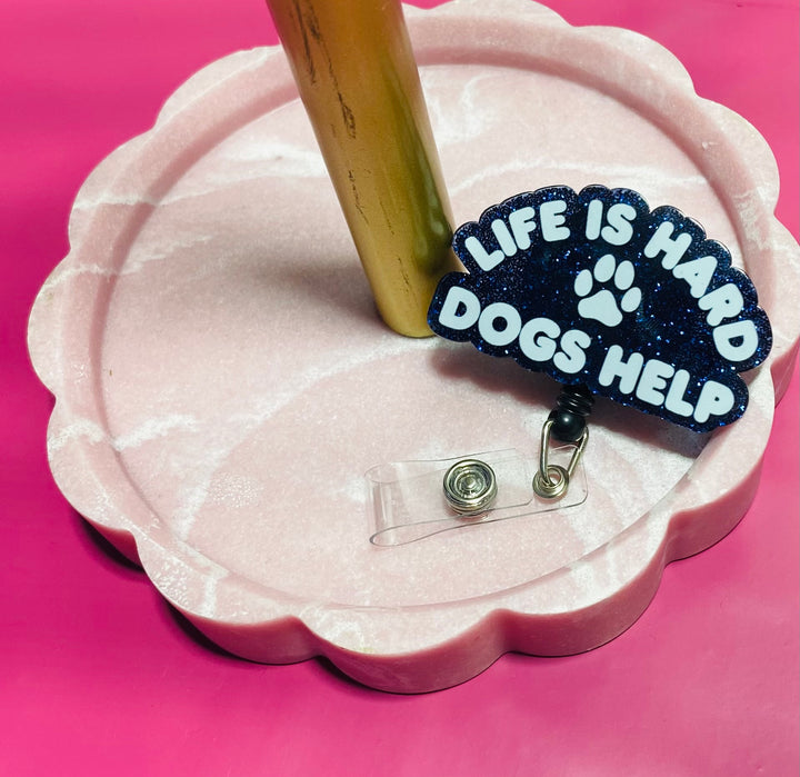 Badge holder with 'Life is Hard, Dogs Help' text on a pink stand against a pink background