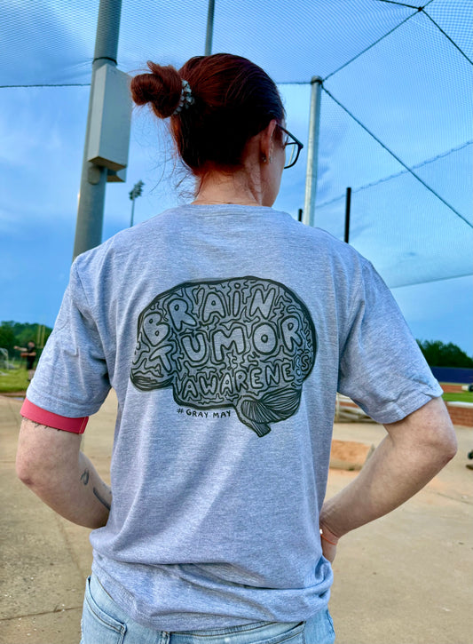 Ladyspinedoc (Dr. Betsy Grunch) showing off the back of her Gray May Brain Tumor Awareness t-shirt showing a graphic brain design with the words “BRAIN TUMOR AWARENESS” and hashtag #GRAYMAY.