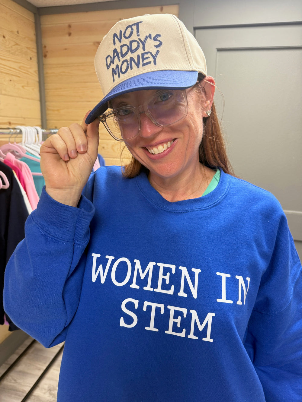 Ladyspinedoc wearing a blue 'WOMEN IN STEM' sweatshirt and a beige cap that says "Not Daddy's Money".