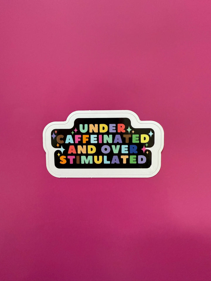 Sticker with colorful text 'UNDER CAFFEINATED AND OVER STIMULATED' on a pink background