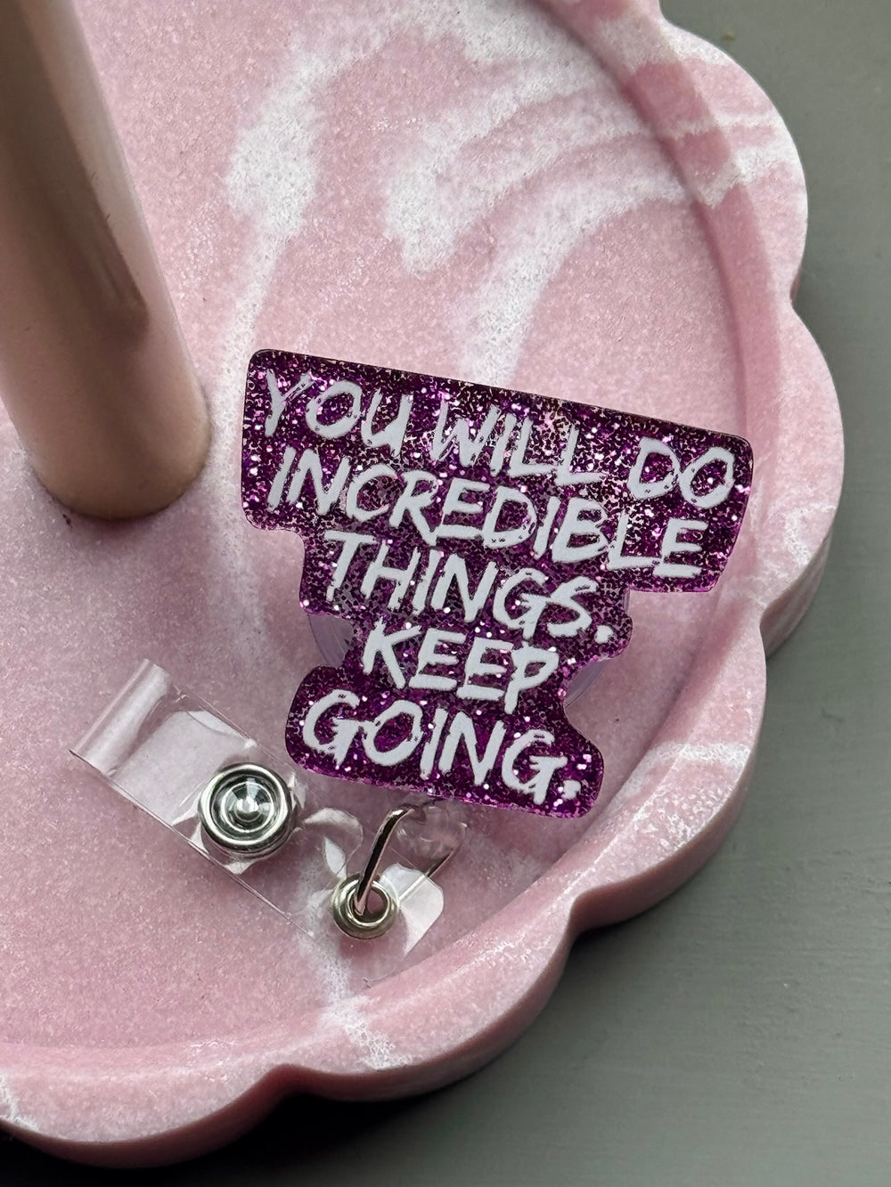 Purple glitter badge reel with the motivational quote “YOU WILL DO INCREDIBLE THINGS. KEEP GOING.” displayed on a pink scalloped tray.