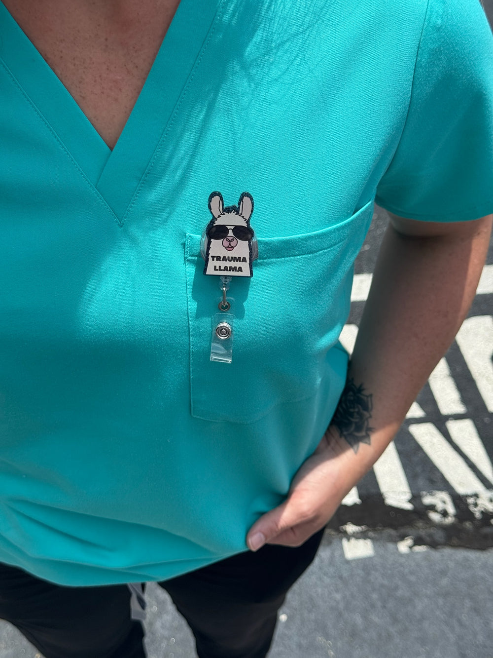 Ladyspinedoc x Dr. Beachgem Trauma Llama Sparkly Badge Reel clipped on front pocket of scrub shirt