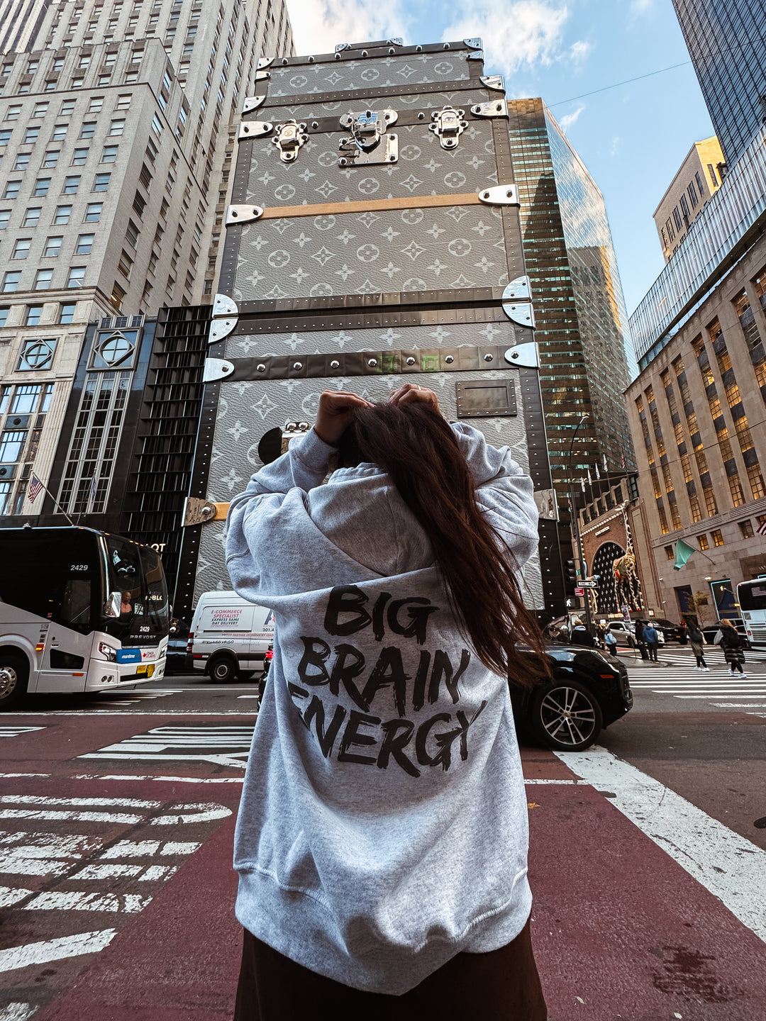 Back of model wearing the light gray BIG BRAIN ENERGY Hoodie in a city environment.
