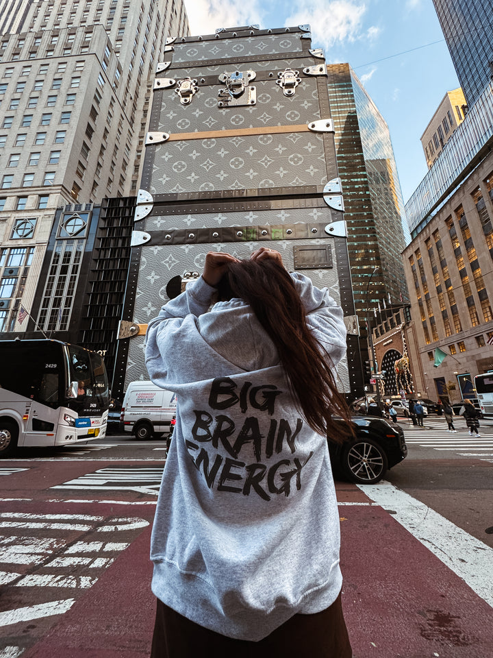 Back of model wearing the light gray BIG BRAIN ENERGY Hoodie in a city environment.
