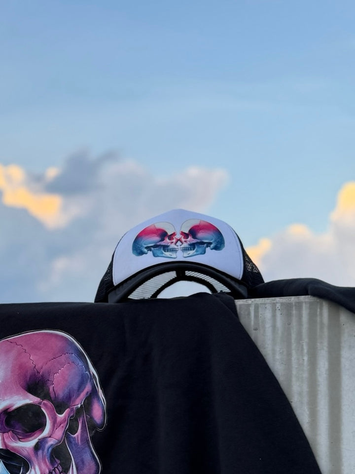 Black and white trucker hat with colorful skulls on the front on top of a black shirt with a matching colorful skull