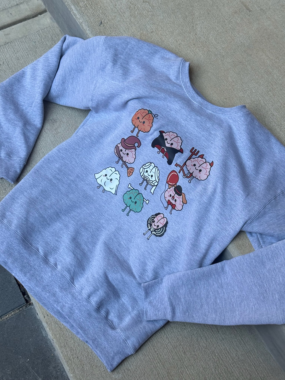 Flay lay of the Gray Halloween Brains Crewneck Sweatshirt with Cartoon Brain Characters: Pumpkin, Ghost, Witch, Vampire, Mummy & More 