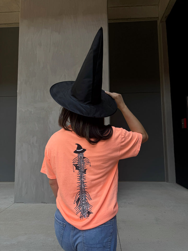 Model in witch hat showing back of Halloween Spooky Spine - Orange Short Sleeve Tee Shirt