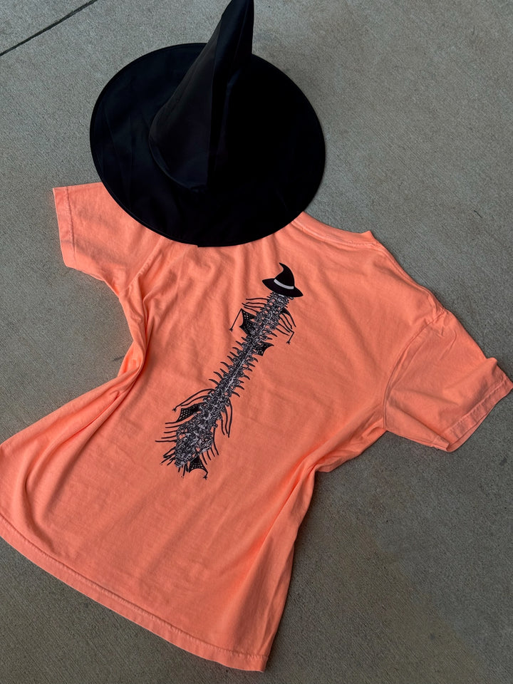 Back flat lay of Halloween Spooky Spine - Orange Short Sleeve Tee Shirt with witch hat next to it