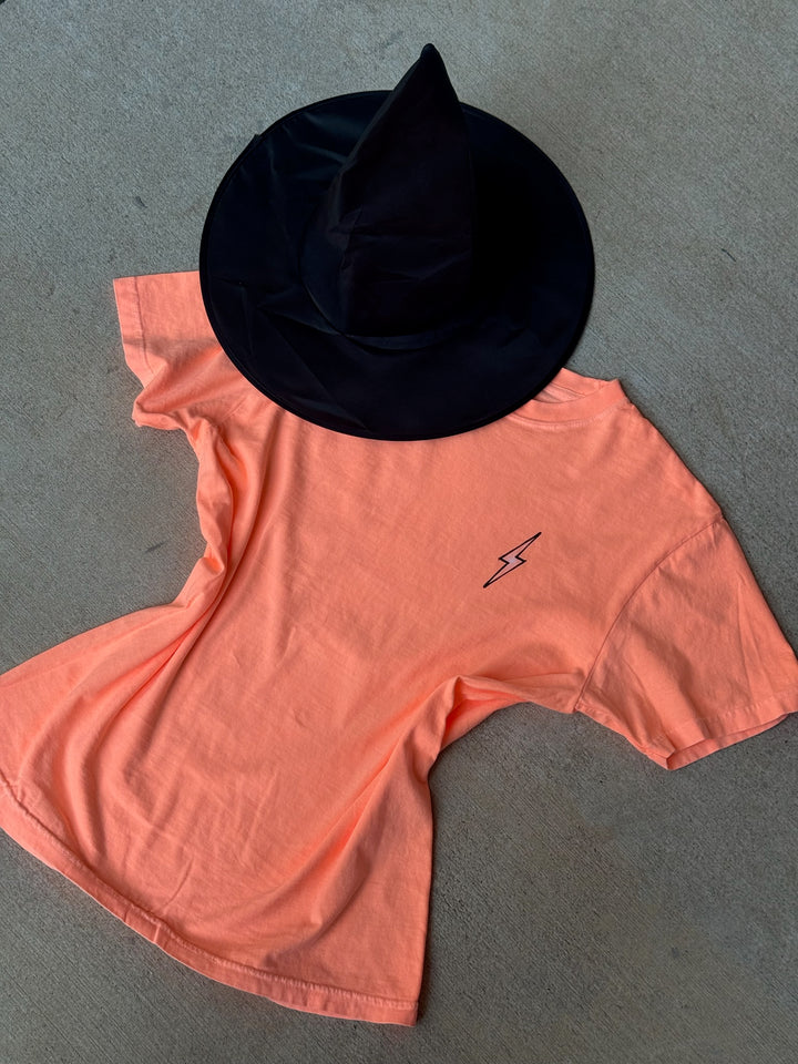 Flat lay of Halloween Spooky Spine - Orange Short Sleeve Tee Shirt with witch hat next to it