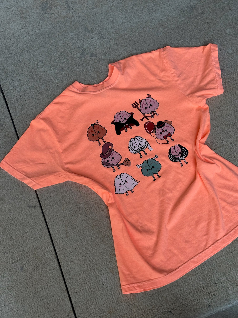 Flat lay of orange Halloween Brains Tee Shirt with Cartoon Brain Characters: Pumpkin, Ghost, Witch, Vampire, Mummy & More