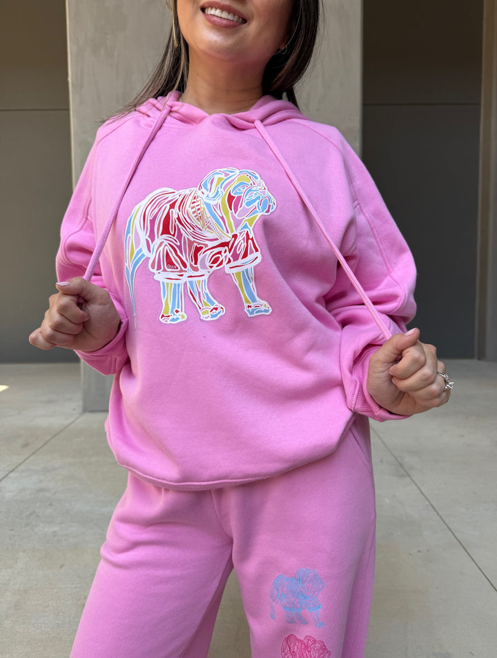 Model wearing Chan Art Collab: Game Day Set - Pink Hoodie & Sweatpants while pulling on the drawstrings of the hoody. Design shows colorful bulldog on front of shirt.