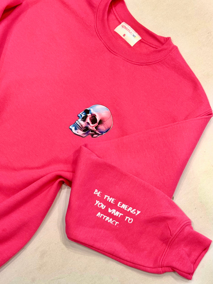 Flat lay of The Power Within Crewneck Sweatshirt - Pink Shirt with Lightning Bolts, Skull, showing Motivational "BE THE ENERGY YOU WANT TO ATTRACT" Motto on sleeve