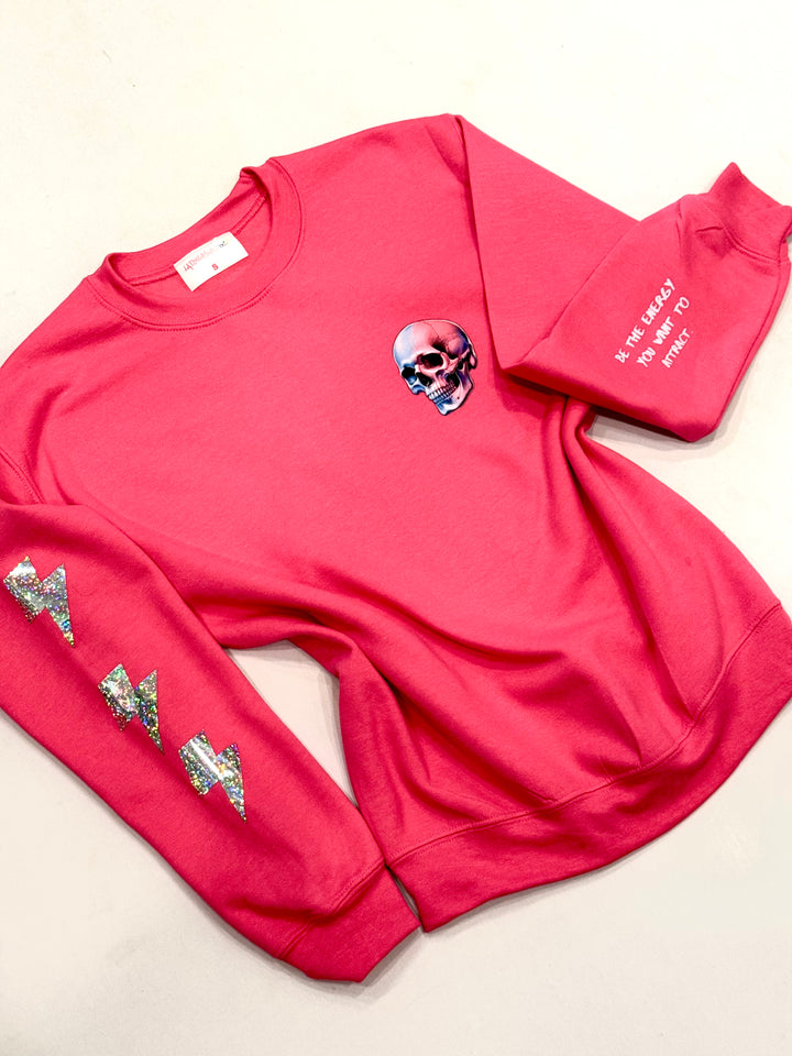 Flat lay of the The Power Within Crewneck Sweatshirt - Pink Shirt with Prismatic Lightning Bolts, Skull, and Motivational "BE THE ENERGY YOU WANT TO ATTRACT" Motto