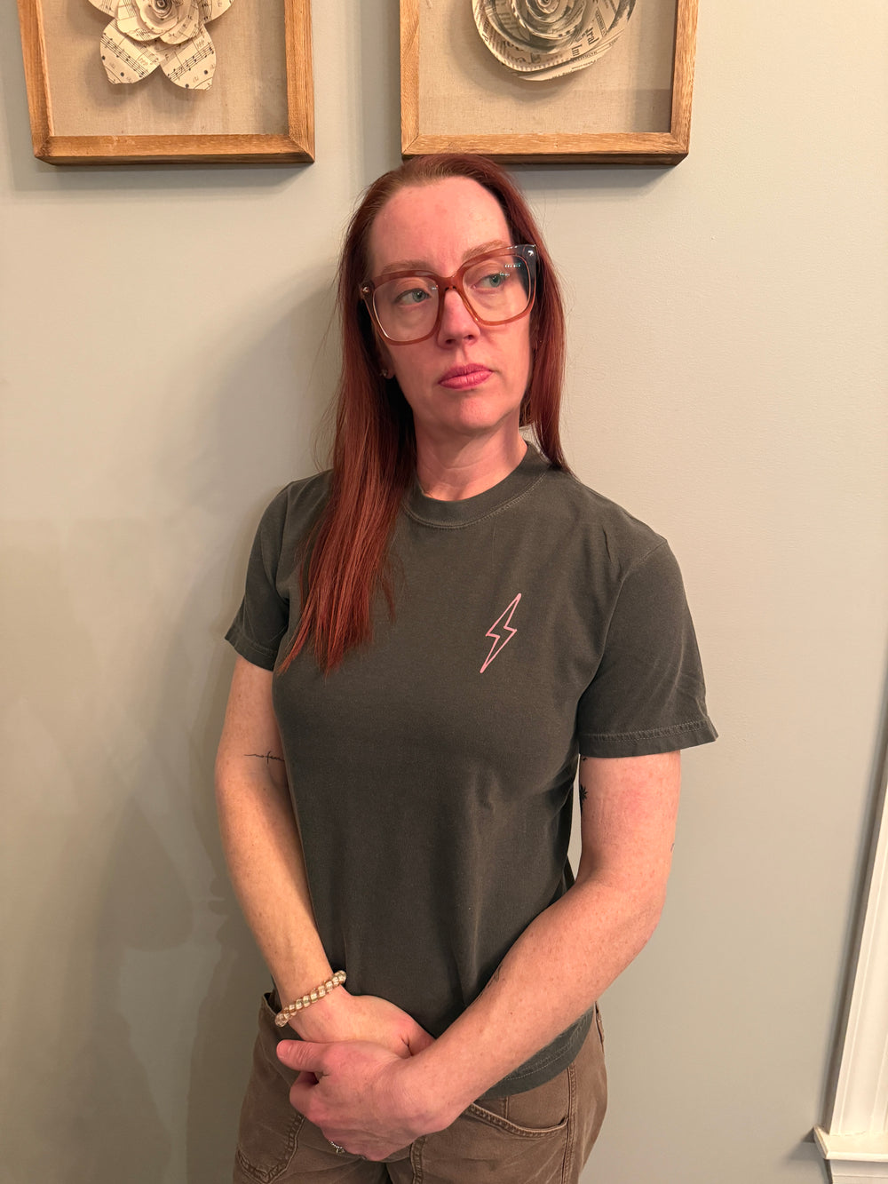 A front view of Dr. Betsy Grunch (Ladyspinedoc) wearing the dark gray Lumbar Puncture tee shirt with her signature lightning bolt on the upper left chest. 