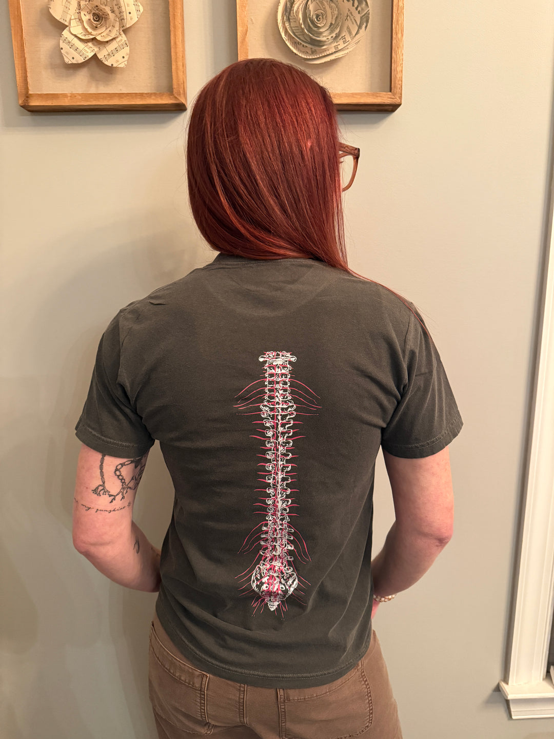 Back view of Dr. Betsy Grunch (Ladyspinedoc) wearing the dark gray Lumbar Puncture tee shirt with spine design.