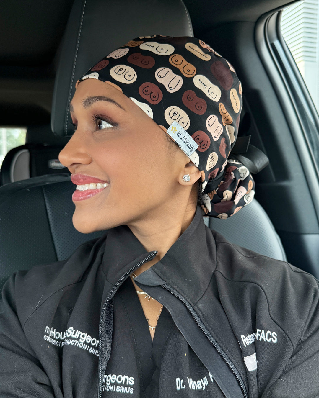 Dr. Rednam (The Confidence Doc) smiling while wearing The Bosom Cap scrub hat, showcasing the unique multicolor breast pattern