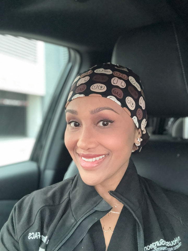 Dr. Rukmini Rednam (The Confidence Doc) wearing The Bosom Cap with a playful boob print design, smiling in her car